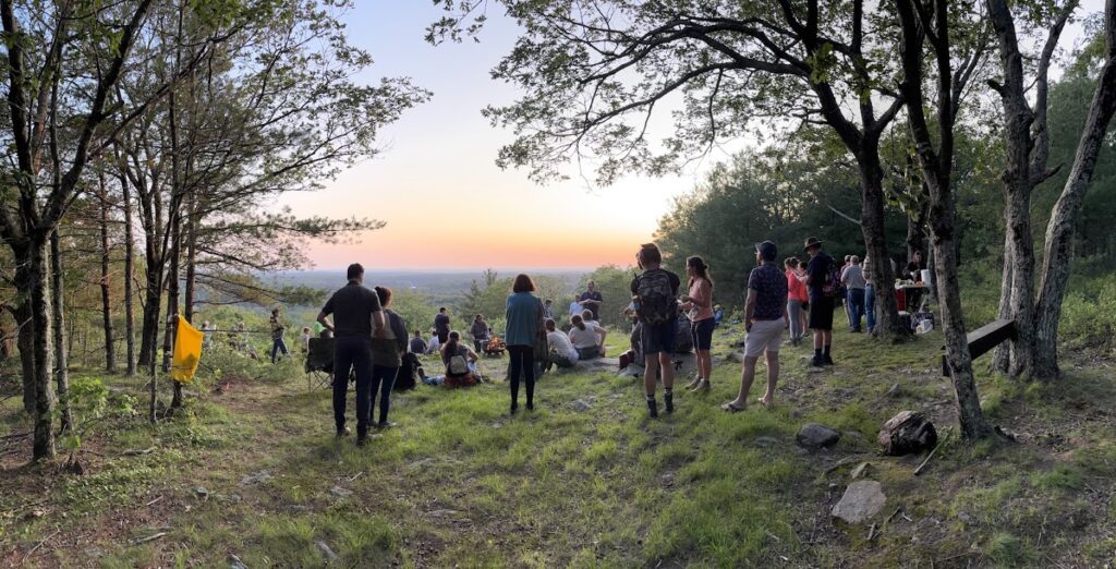 A group of people watch the summer solstice sunset from Thoreau's Seat.